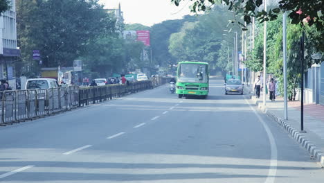 green city bus drives on a quiet afternoon street in bangalore with sparse traffic and trees around