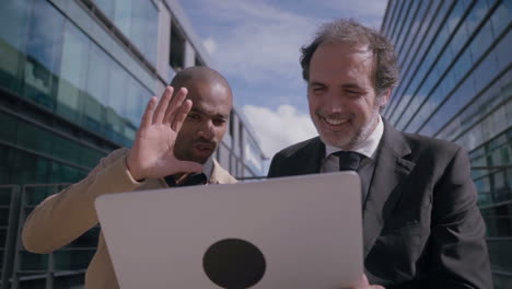 multiethnic coworkers having video chat on laptop outdoors