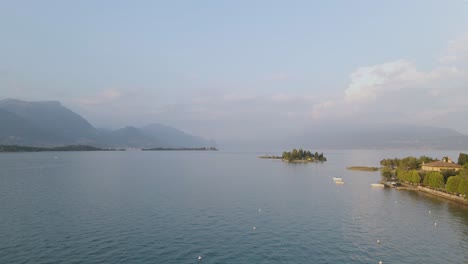 Vista-Aérea-Sobre-El-Costo-Del-Lago-De-Garda-Y-La-Isla-De-San-Biagio-Por-La-Ciudad-De-Manerba,-Italia