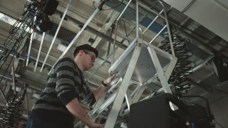 studio worker climbing ladder adjusting lights, preparing for production in broadcast environment, technician adjusting equipment during studio setup, professional production lighting