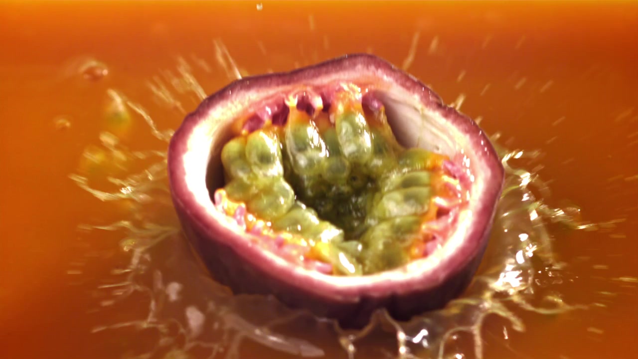 Frisk passionsfrugthalvdel plasker ned i appelsinjuice i slow motion