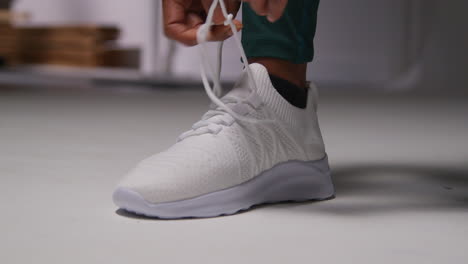 close up of female athlete in gym or changing room tying laces of training shoe before exercising