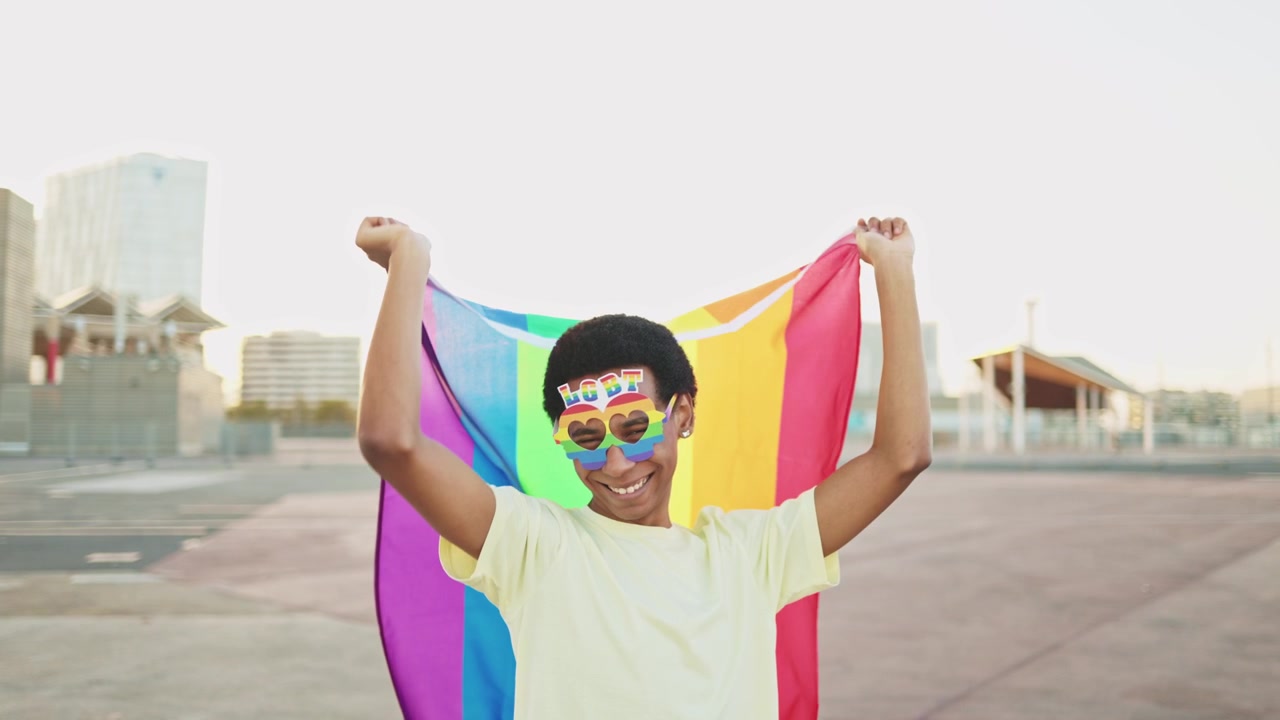 Happy Young Person Holding Rainbow Flag and Wearing Pride Glasses