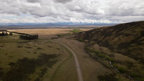 Aerial:-Car-driving-on-desert-road-with-snow-capped-mountains-in-background