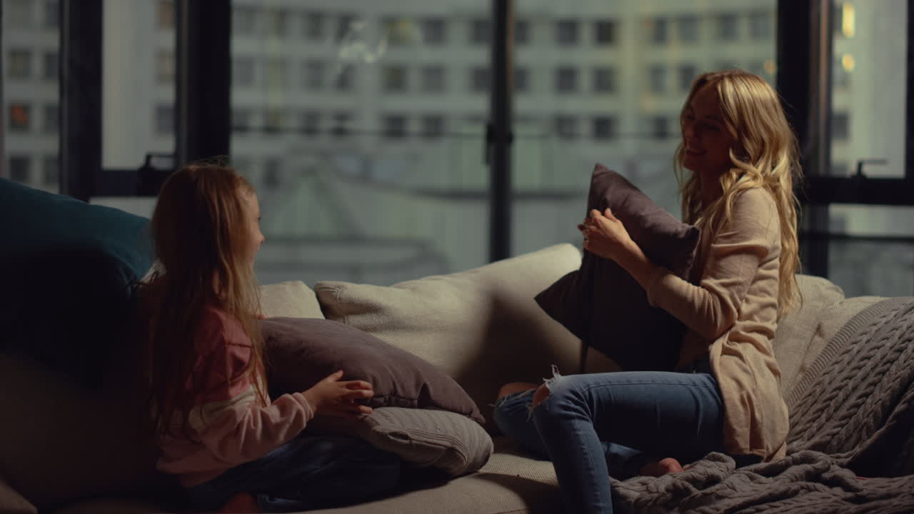 Happy mother and daughter having pillow fighting. Mom kid girl playing indoors.