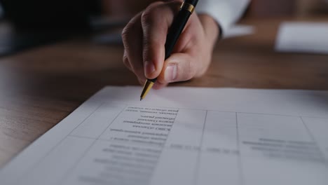 Close-up-a-guy-in-a-white-shirt-writes-his-signature-with-blue-ink-on-a-white-sheet-of-document-using-a-black-pen-in-the-office