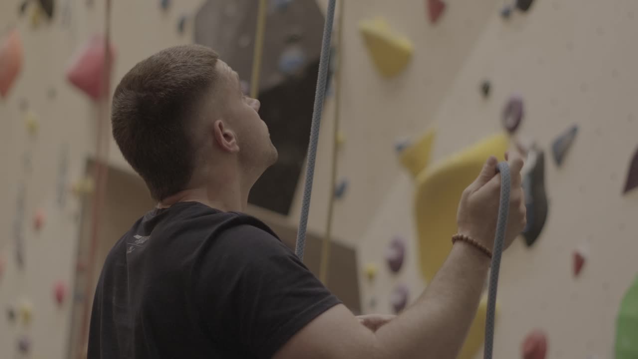 hombre asegurando la cuerda en una instalación de escalada cubierta, escalador preparando equipo en el gimnasio