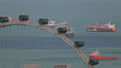 singapore - 5 march 2025 : container ships waiting in the sea by singapore with observation ferris wheel in foreground
