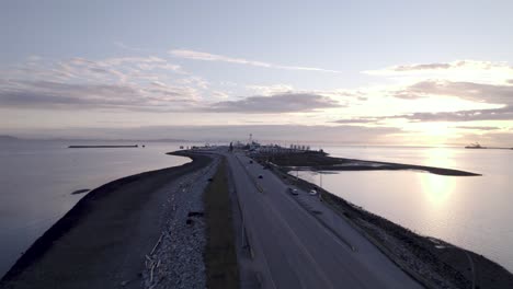 tsawwassen ferry port in british columbia, drone fly above highway over the ocean water during sunset with traffic car driving through the port, vancouver canada