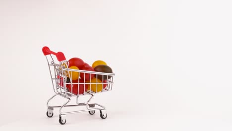 un carrito de supermercado en movimiento lleno de tomates de uva multicolores. aislados en el fondo blanco. primer plano. macro.