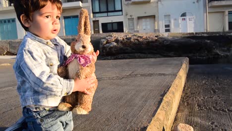 lindo niñito en jeans jugando con su conejito marrón con luz del atardecer