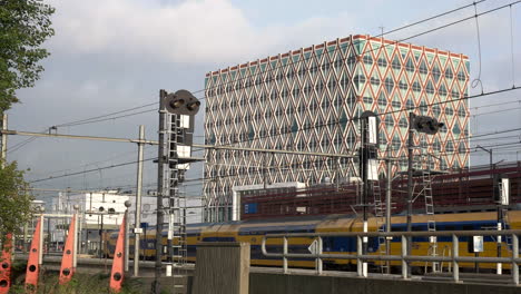 Gelber-Zug-Fährt-Am-Bahnhof-Gouda-Mit-Rathausgebäude-Im-Hintergrund-In-Den-Niederlanden