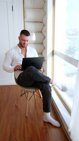 man sitting his leg on the leg holding a laptop. happy relaxed person working online from home. vertical video.