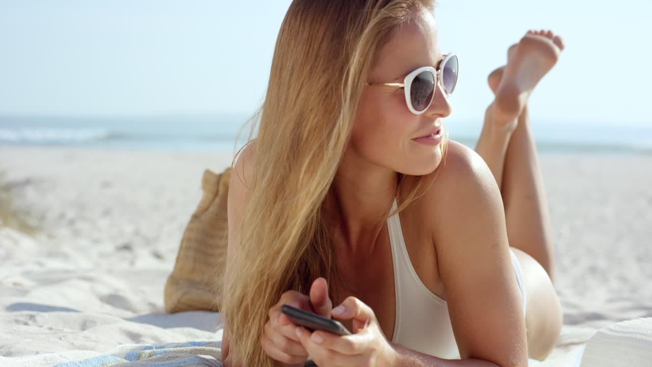 beautiful woman using phone text messaging conversation lying on beach suntanning