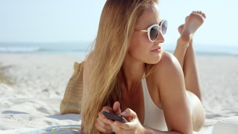 Hermosa-Mujer-Usando-Conversación-De-Mensajes-De-Texto-Telefónico-Tumbado-En-La-Playa-Bronceándose