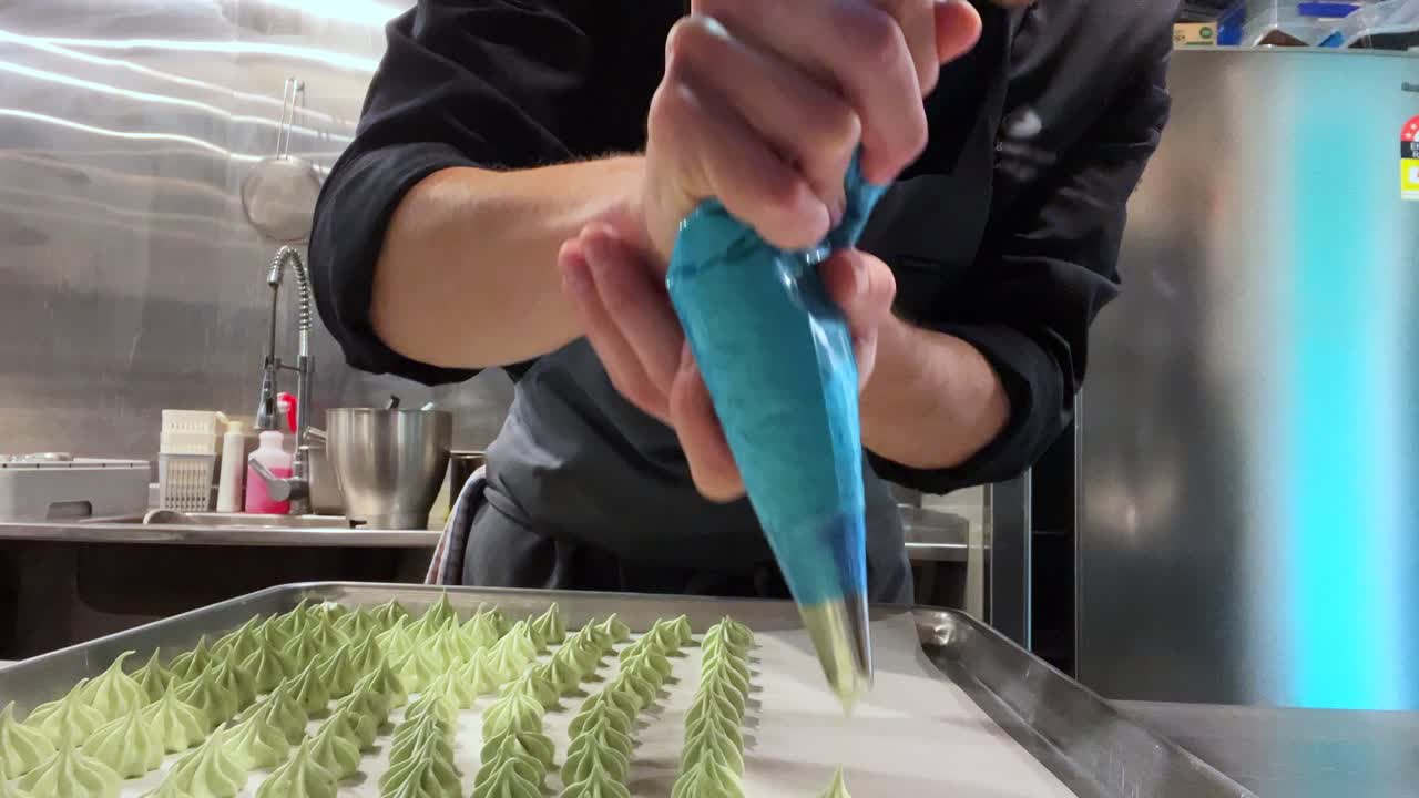 joven chef usando bolsa de tubería para hacer un gran lote de merengue verde