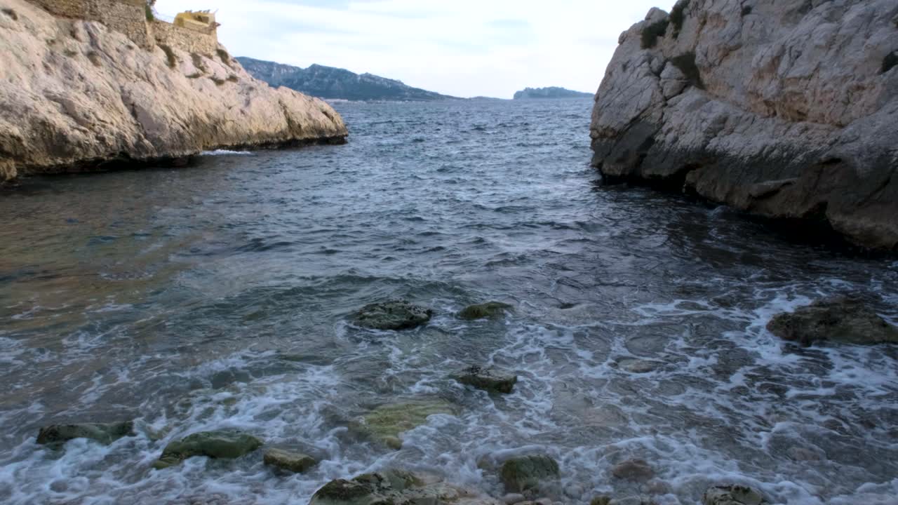Středomořské vlny se tříští mezi skalnatými okraji Marseille na klidnou oblázkovou pláž