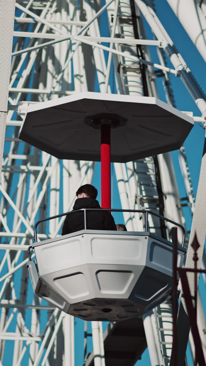 Close up of people in a cabin in a Ferris Wheel with the blue sky on the background. Vertical