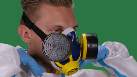 vista lateral de un médico de sexo masculino en un traje de protección blanco y guantes quirúrgicos pone un respirador médico. pantalla verde, tecla de croma. cámara lenta. primer plano