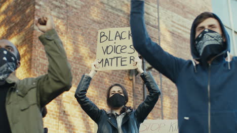 caucasian woman with scarf on her face yelling and holding black voices matter" signboard in a protest with multiethnic group of people in the street"