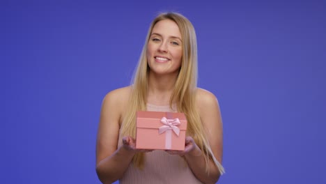 hermosa mujer sonriente está sosteniendo una caja de regalos a la cámara frente a la pantalla azul