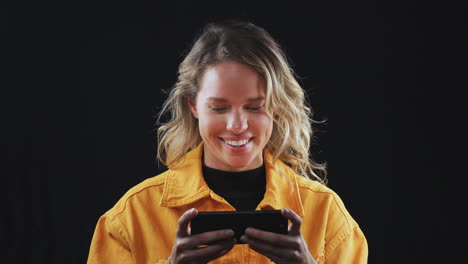Studio-Shot-Of-Woman-Playing-Game-On-Mobile-Phone-And-Smiling-In-Slow-Motion
