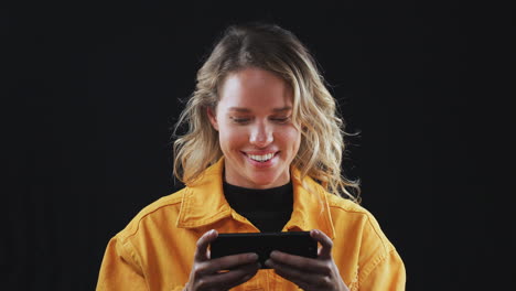 studio shot of woman playing game on mobile phone and smiling in slow motion