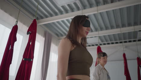 balanced souls blindfolded their eyes while standing still inside calm yoga studio, gently pausing during meditative practice surrounded by soft window light in peaceful environment