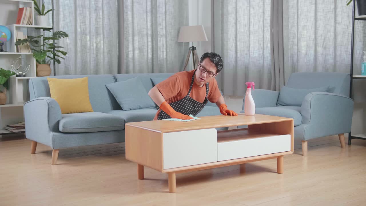 집에서 스프레이로 테이블을 청소하는 동안 등통을 겪는 아프론을 입은 아시아 남성 집사