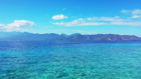 blue calm ocean with cloudy blue sky above, mare island, indonesia - aerial shot