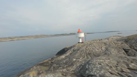 dangerous low altitude flying over rocky island toward small lighthouse, fpv drone