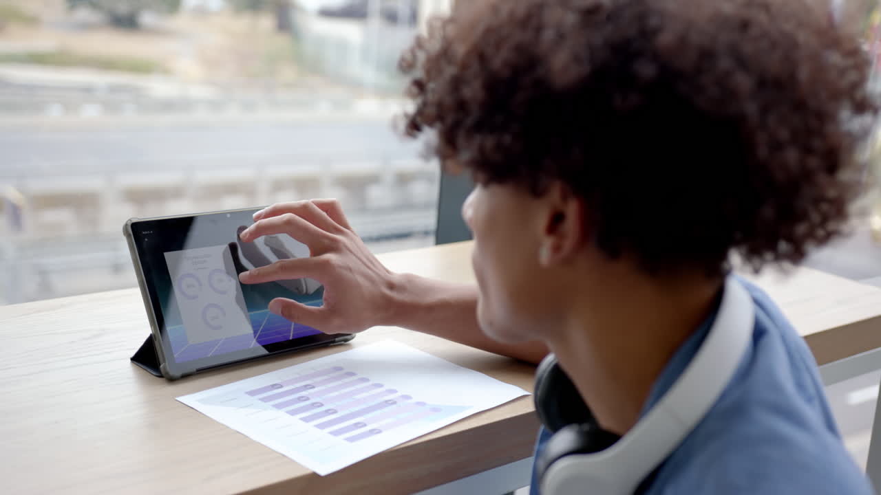 Using tablet, man analyzing data charts with headphones on desk