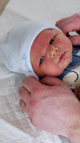 unrecognized dad putting a cap on tiny baby. newborn baby in blue romper is dressed by father. top view. vertical video