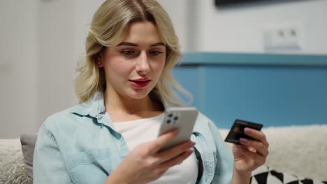 happy young woman holding credit card using instant mobile payments at home