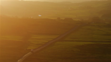 long lens drone shot of lorry driving along road in the yorkshire dales at sunset through the haze