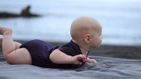 with the ocean in view, the baby lies on his stomach on the black sand, joyfully laughing as he connects with the camera