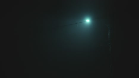gimbal low angle shot of lit blue light pole in foggy night