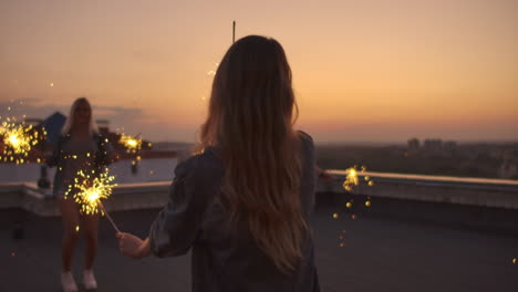 la hembra en el techo mueve sus brazos y cuerpo hermosamente y baila con sus amigas en una noche de verano con una gran luz bengal. su cabello sopla hermosamente en el viento antes de la noche.