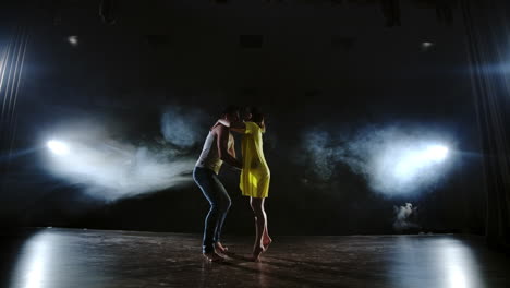 zoom camera two modern ballet dancers are dancing on stage in smoke a man raises his partner in his arms and rotates in the air. the musical uses circus acrobats dancers.