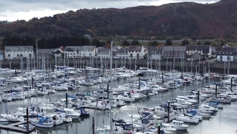 Scenic-luxurious-waterfront-harbour-apartment-village-yachts-and-sailboats-under-mountain-coastline-rising-establishing-aerial-view