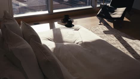 sun shades rising to reveal a bed with white bedding and a bedside tray that includes 2 coffee mugs and a book in a luxury bedroom