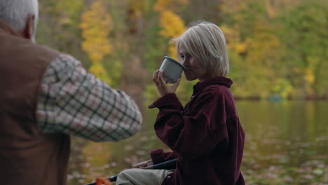 a young girl enjoys a warm drink outdoors with an older man by a lake in autumn