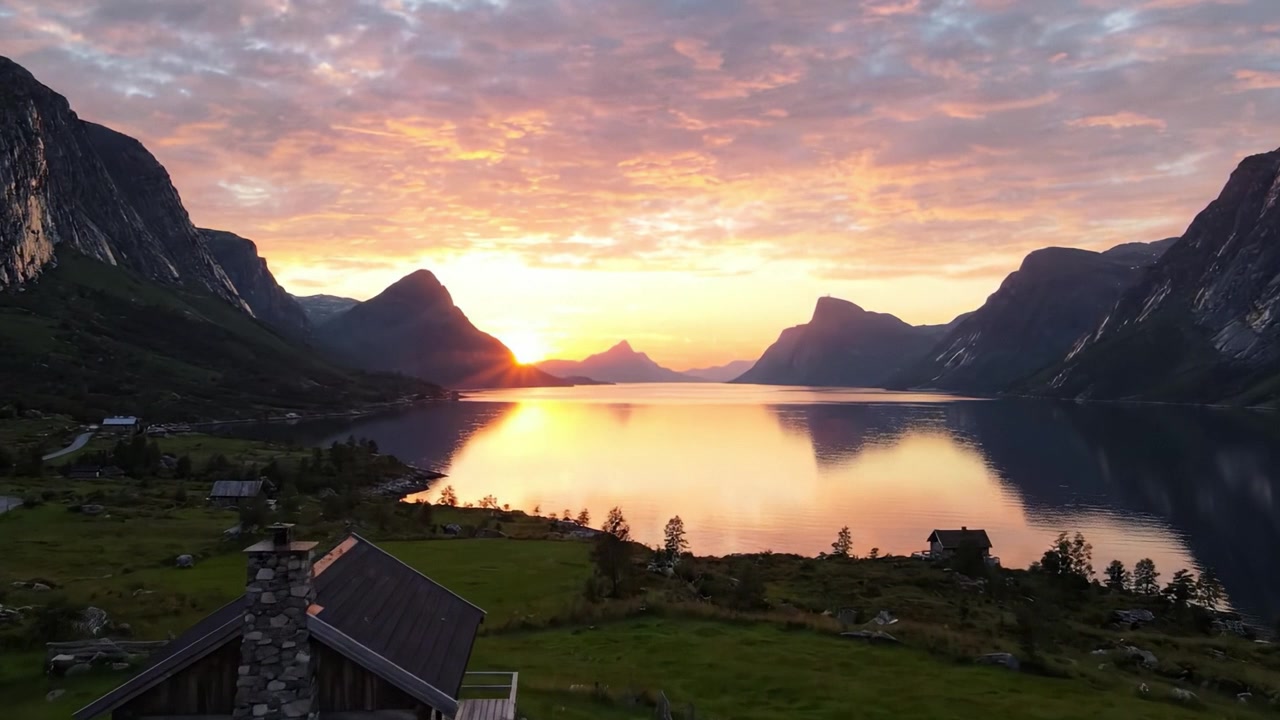 Betagende solnedgang over en fredfyldt sø omgivet af majestætiske bjerge og en rolig hytte, der fanger naturens skønhed i et malerisk landskab.