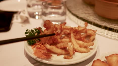 chopsticks lift stir-fried fish from a plate in a warmly lit restaurant, showcasing culinary presentation and dining ambiance