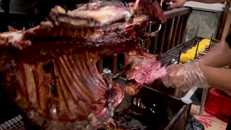 a chef's hand is cutting goat meat from grilled goat