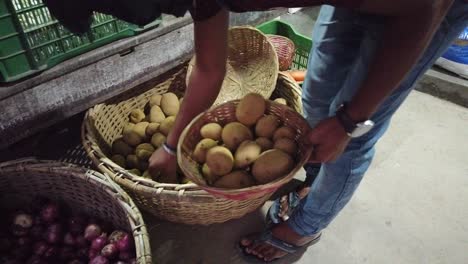 a man a the market picks out potatoes from his main basket into a smaller basket for his client