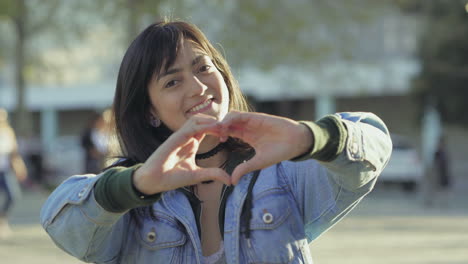 una adolescente sonriente haciendo forma de corazón con las manos