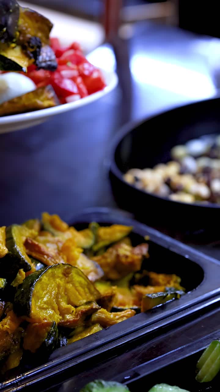 Primo piano di un cliente che usa le pinze per servirsi zucca arrosto a un buffet di insalate ben illuminato