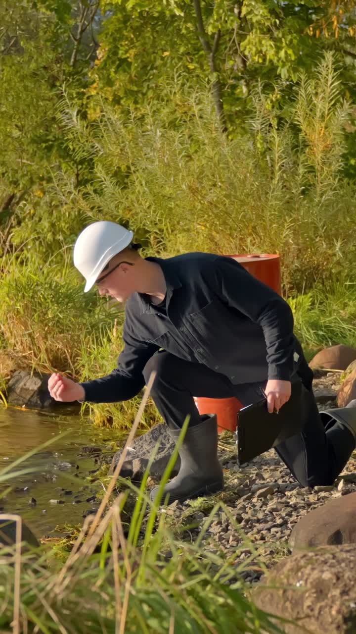 Scientist crouches down inspecting water sample from stream during fieldwork, vertical