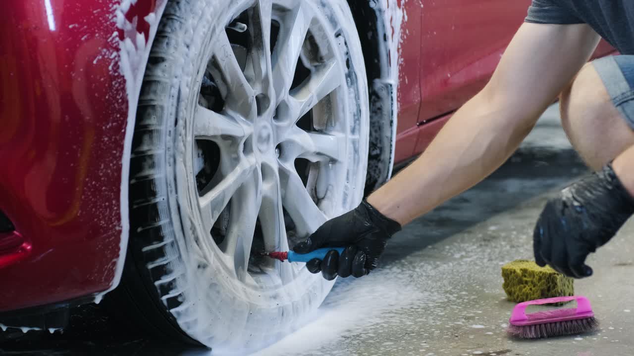hombre trabajador lavando las ruedas de aleación del coche en un lavado de coches